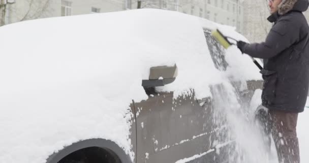 Mannen i varma kläder rengör sin bil från snö — Stockvideo