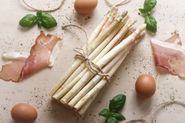 Beyaz arka planda kuşkonmaz, yumurta, fesleğen ve jambon.