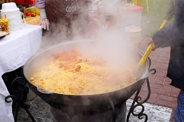 Sokak yemeği festivalinde pilav pişirmek. Aşçı pilavı bir kürekle karıştırır. Kazan, Eylül 2021