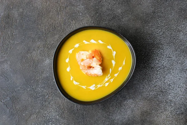 Traditional pumpkin soup with creamy texture and shrimps on a dark background