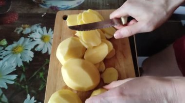 Kadın patatesleri kesme tahtasından kesiyor, yakın plan, 4K video.