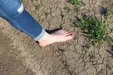 Kırık zeminde ve çimenlerin üzerinde kot pantolon giymiş bir kadın.