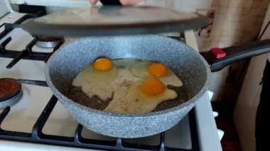 Aşçı çırpılmış yumurtalarla bir tava açar, kapağı gösterir ve kapatır