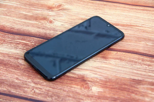 Ahşap arka plana yansıyan tuğla duvarlı siyah ekranlı akıllı telefon.