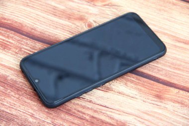 Ahşap arka planda baş aşağı duran siyah akıllı telefon.