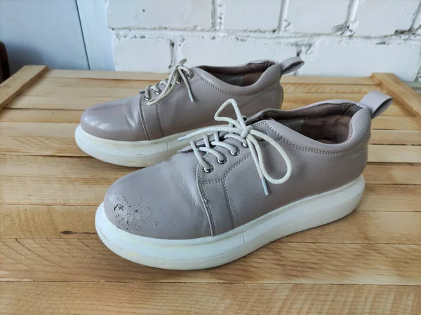 Beige female patent leather platform sneakers on the wooden background