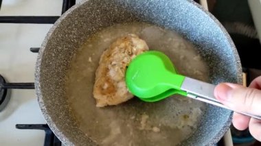 Adam tavada kızartılmış tavuk göğsünü çeviriyor.