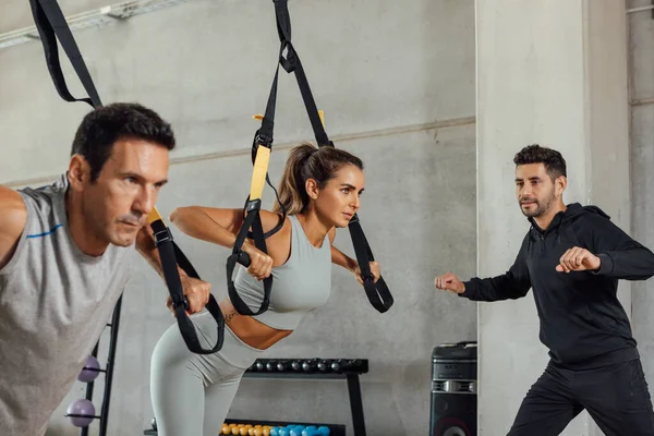 Woman and man do suspension push ups training with a coach at a fitness club.