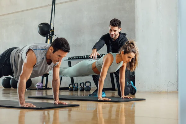 Entrenador personal ayuda a hacer la posición de tablón a una pareja de fitness. — Foto de Stock