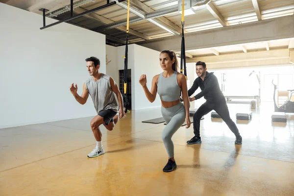 Deportivo hombre y mujer entrenar ejercicio de embestida con bucles funcionales en el gimnasio. — Foto de Stock