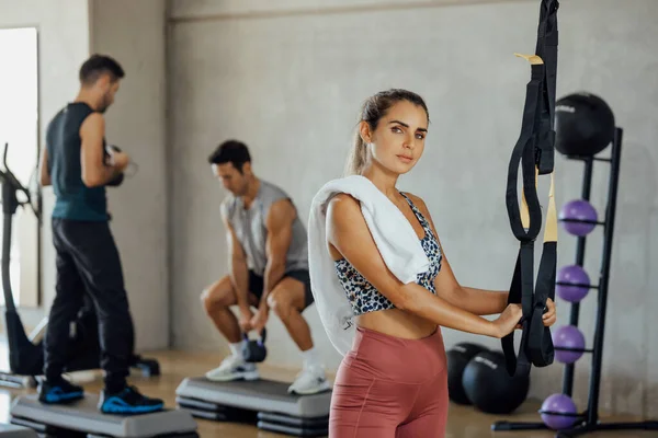 Mujer Fitness Confianza de pie en el gimnasio con dos hombres haciendo ejercicio en la espalda. — Foto de Stock