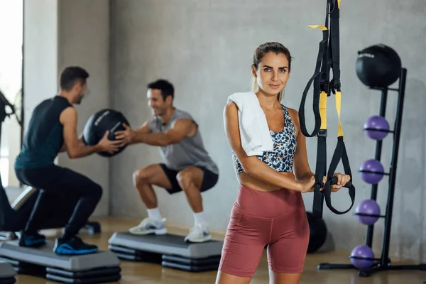 Selbstbewusste Fitness-Frau steht mit zwei Männern im Fitnessstudio und trainiert im Rücken. — Stockfoto