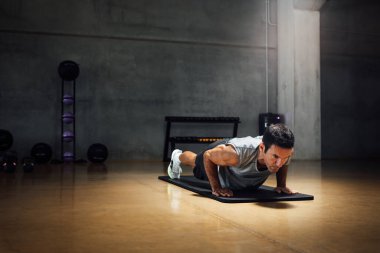 Kafkasyalı güçlü bir adam aşağı bakar şınav, tahta duruşu, karanlık bir spor salonunda.