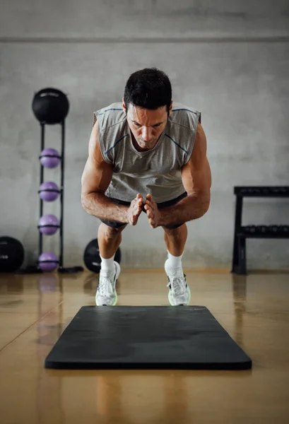 Strong fitness man jumps while does push-ups in gym.