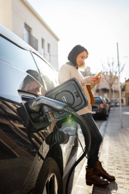 Barselona sokaklarında elektrikli araba bekleyen bir kadın.