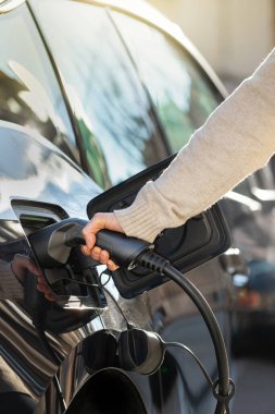 Kırpılmış manzaralı kadın elektrikli arabayı şarj etmek için fiş takıyor.