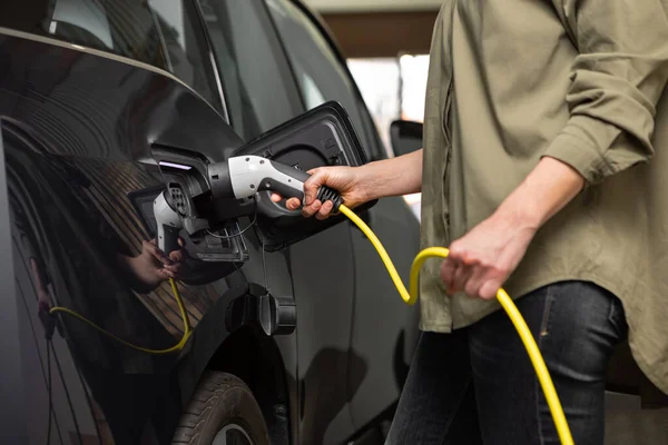 Close-up van vrouw opladen elektrische auto met kabel in garage thuis — Stockfoto