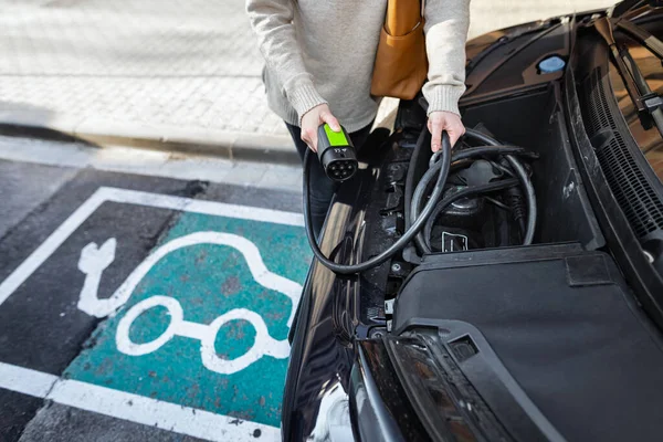 Gesneden vrouw plukken kabel van een elektrische voorste kofferbak auto op te laden voertuig — Stockfoto