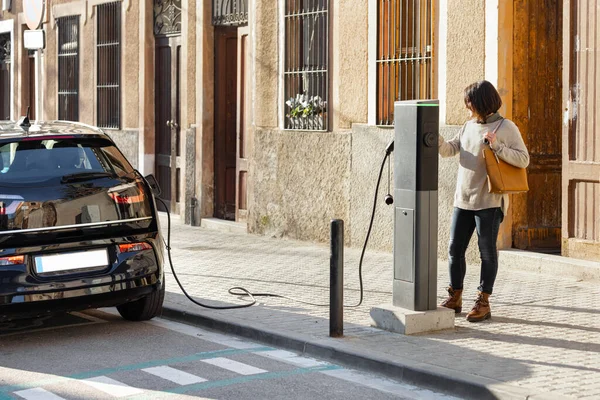 Vrouw in de buurt van een oplaadstation om haar elektrische auto op te laden. — Stockfoto