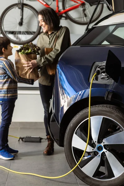 Gelukkig gezin haalt de boodschappen terwijl elektrische auto is opladen thuis. — Stockfoto