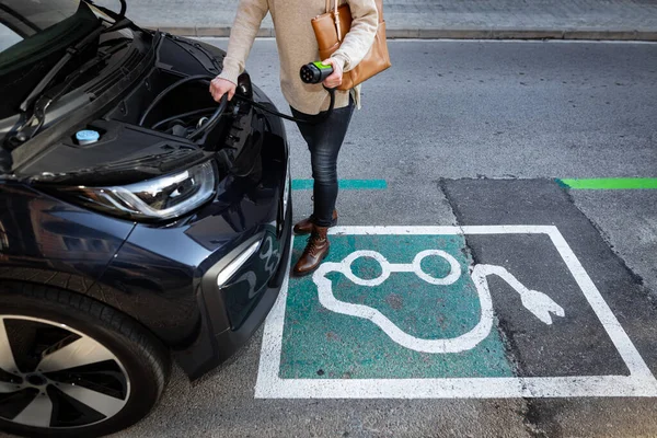 Gesneden vrouw plukken kabel van een elektrische voorste kofferbak auto op te laden voertuig — Stockfoto