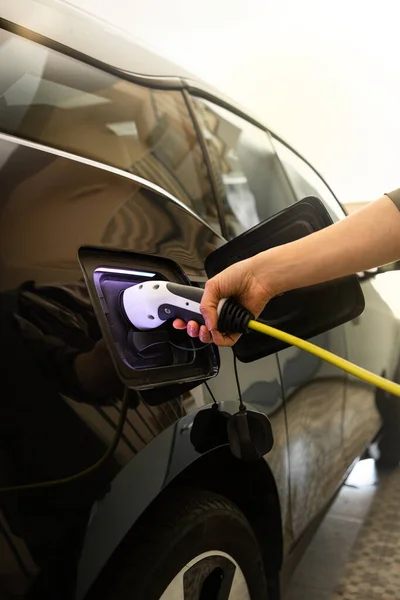 Close-up van vrouwelijke hand pluggen een lader om elektrische auto stopcontact thuis. — Stockfoto