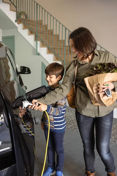 Moeder en zoon opladen elektrische auto thuis. — Stockfoto
