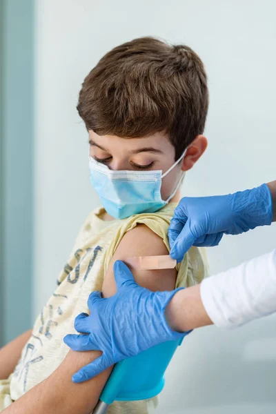Las enfermeras con guantes ponen una tirita en el brazo de un niño después de la vacunación.. —  Fotos de Stock