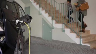 Belli bir garajda elektrikli bir aile arabasını şarj eden kablolu yayın..