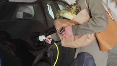 Kadın marketten alışveriş yaptıktan sonra şarj aletini elektrik prizine takıyor..