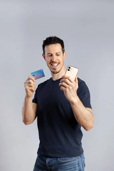 Hombre sonriente utiliza teléfono inteligente y tarjeta de crédito azul. —  Fotos de Stock