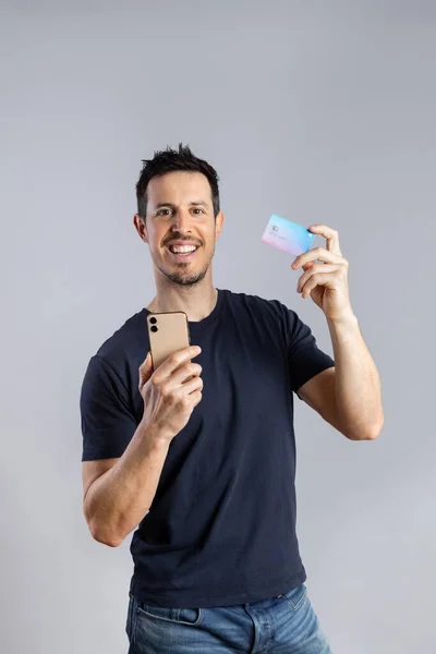 Hombre sonriente utiliza teléfono inteligente y tarjeta de crédito azul. —  Fotos de Stock