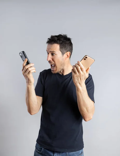 Hombre desesperado sostiene dos teléfonos inteligentes, grita a su teléfono celular. —  Fotos de Stock
