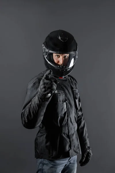 Studio shot of Motorcyclist biker in black equipment points and looks at camera. — Stock Photo, Image