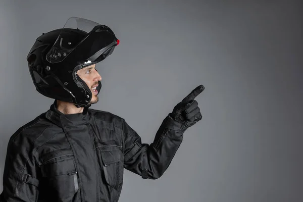 Man wearing protective black motorcycling equipment, pointing a side, indoors. — Stock Photo, Image