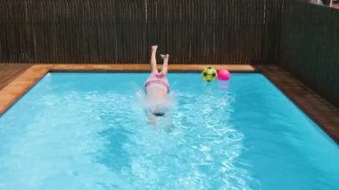 Çocuk Mavi Su Havuzu 'na atlıyor ve berrak su sıçrıyor. Çocuk güneşli bir günde suyun altında yüzüyor. Çocuk yaz tatilinde dinleniyor. Yavaş çekim