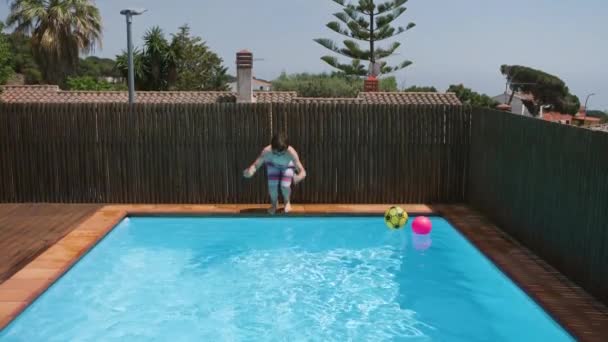 少年は青い水プールに飛び込み 青い澄んだ水を撒き散らします 子供は晴れた日に水中で泳ぐ 少年は夏休み中にリラックスします スローモーション — ストック動画