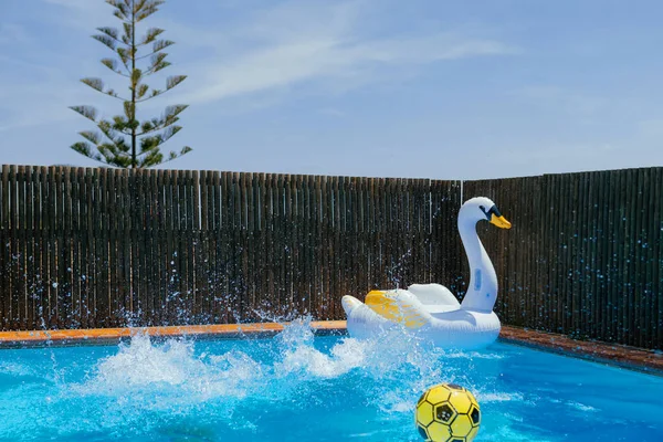 Splashing water in a private pool in a house backyard. Two kids jumped in a pool with inflatable swan and yellow ball. Summer, recreation, holidays, vacation.