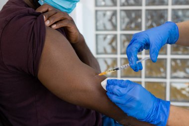 Bir hastane ya da klinikteki koruyucu mavi eldivenli bir sağlık görevlisinden Covid-19 'a karşı aşı olan siyahi bir adam. Yatay