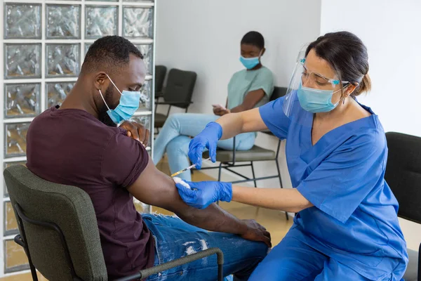 Kvinnlig Läkare Skyddsuniform Latexhandskar Och Ansiktsskydd Vaccinerar Unga Manliga Afroamerikanska — Stockfoto
