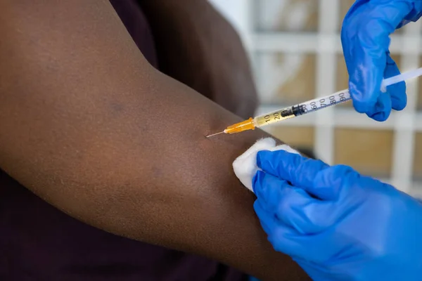 Close-up of injection needle syringe. Hands in protective gloves applying on a black male patient. Cropped of black man receiving vaccine shot. Horizontal