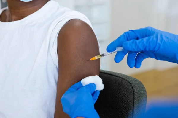 Close-up of injection needle syringe. Hands in blue protective gloves applying on a black female patient with turned up sleeve. Cropped of black woman receiving vaccine shot. Horizontal