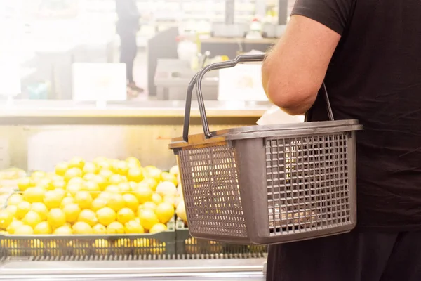 Man with empty grocery basket in hypermarket near fruit display case, soft focus