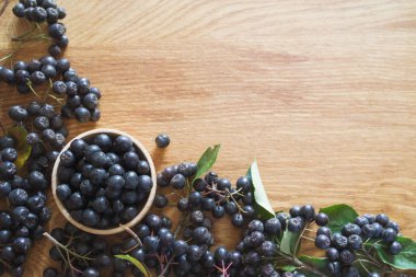 Yaban mersini, ahşap yuvarlak bir kasenin içinde ve etrafında, üst manzara, kopyalama alanı. Siyah meyveli dağ külleri - bir sonbahar arkaplanı