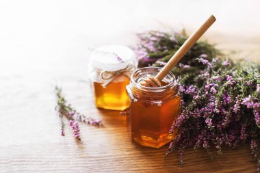 Cam kavanozdaki Heather balı ve tahta bir masa yüzeyindeki bir demet orman keneviri çiçeği. Yumuşak seçici odak, kopyalama alanı. Alternatif tıp