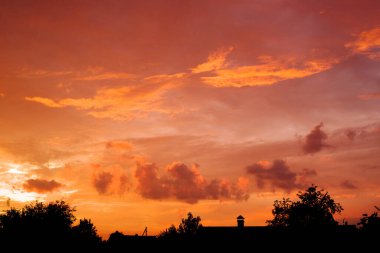 Güneş doğmadan önce kırmızı ve turuncu bulutlu gökyüzü kırsal çatı ve ağaçların siyah silolarına karşı. Dawn Sky ile Ağustos Manzarası