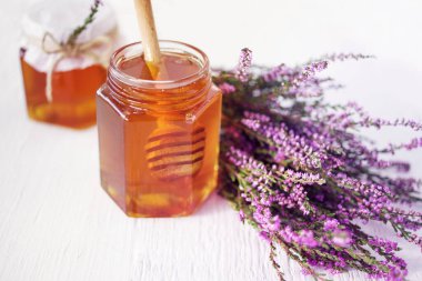 Cam kavanozda Heather Bal ve beyaz masa yüzeyinde bir demet orman keneviri çiçeği, yumuşak seçici odak. Alternatif tıp