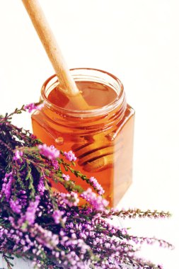 Cam kavanozda Heather Bal ve beyaz masa yüzeyinde bir demet orman keneviri çiçeği, yumuşak seçici odak. Alternatif tıp