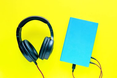 Mavi bir kapak ve parlak sarı arka planda siyah kulaklıklar, üst manzara, yakın çekim. Bir sesli kitabı, okumayı, eğitimi dinlemenin kavramsal görüntüsü