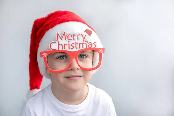 クリスマスの赤い帽子と休日の眼鏡でかわいい笑顔の男の子 光の背景 コンセプトクリスマス 新年の雰囲気 — ストック写真